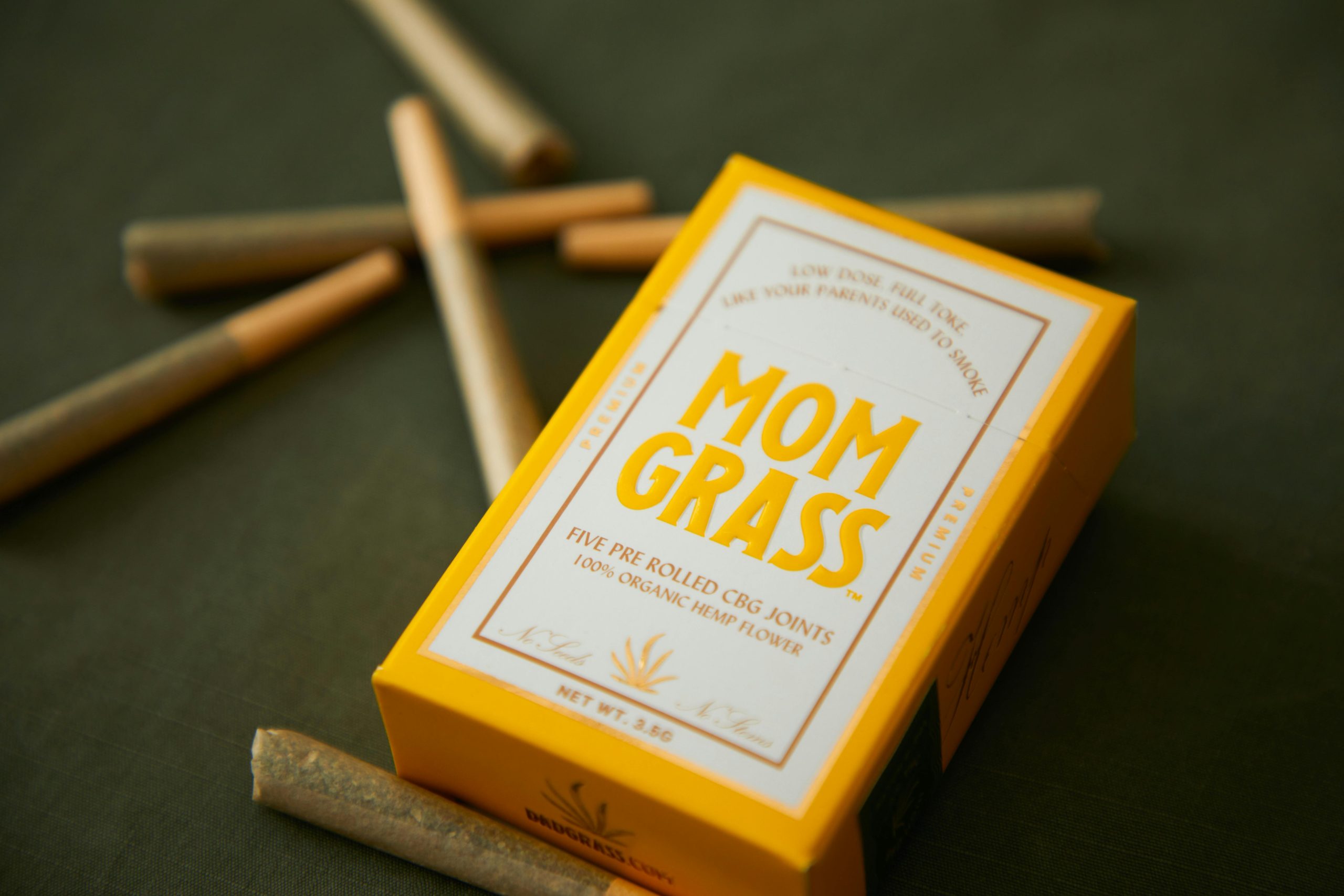 Close-up of Mom Grass CBG joints packaging with loose joints on a surface.